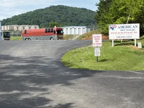 Paved entrance driveway and roadside sign at American Mini Storage, 176 National Ave, Staunton VA, with an RV parked beside the storage buildings